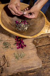 Hands of woman crushing herbs in wooden bowl at table - DAWF01850