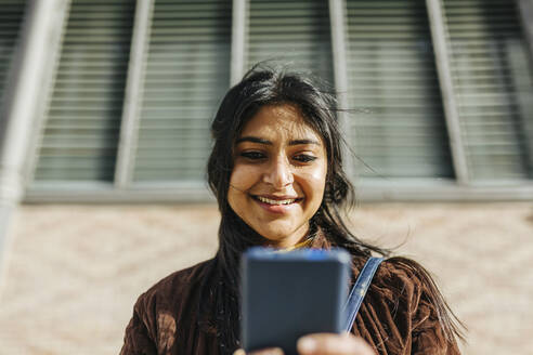 Smiling woman using mobile phone against building - XLGF01219