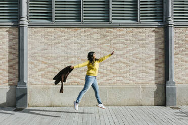 Frau mit Jacke springt auf dem Gehweg an der Mauer - XLGF01222