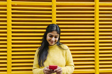 Frau mit Mobiltelefon an gelber Wand stehend - XLGF01223