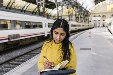 Frau schreibt in ein Buch, während sie auf dem Bahnsteig steht - XLGF01231