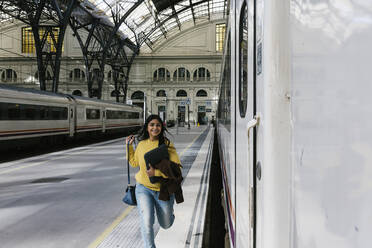 Lächelnde Frau mit Laptoptasche läuft auf dem Bahnsteig, um den Zug zu erreichen - XLGF01237