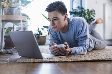 Young man holding coffee cup while watching video on laptop - UUF22766