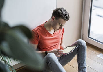 Young man using digital tablet while sitting against wall - UUF22779