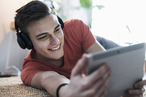 Lächelnder junger Mann mit drahtlosen Kopfhörern, der ein Video auf einem digitalen Tablet anschaut - UUF22780
