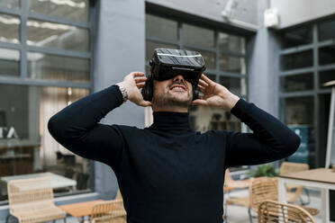 Lächelnder Geschäftsmann, der ein Virtual-Reality-Headset benutzt, während er in einem Café sitzt - EGAF01913