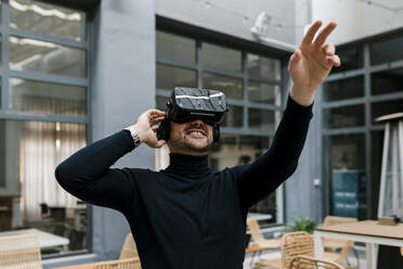 Geschäftsmann streckt seine Hand aus, während er ein Virtual-Reality-Headset in einem Café benutzt - EGAF01914