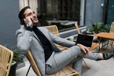 Mid adult businessman talking on mobile phone while sitting at cafe - EGAF01916