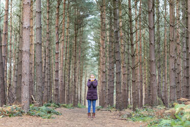 Frau in warmer Kleidung inmitten von Bäumen im Wald stehend - WPEF04181