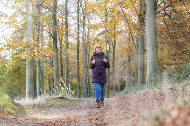 Lächelnde Frau mit Rucksack schaut weg, während sie im Herbst im Wald spazieren geht - WPEF04187