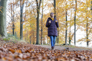 Lächelnde Frau, die einen Rucksack hält und im Herbstwald nach oben schaut - WPEF04188