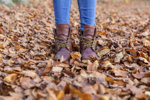 Woman in boots standing in autumn leaves while hiking in forest - WPEF04190