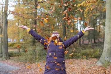 Cheerful woman playing with autumn leaves in forest - WPEF04191