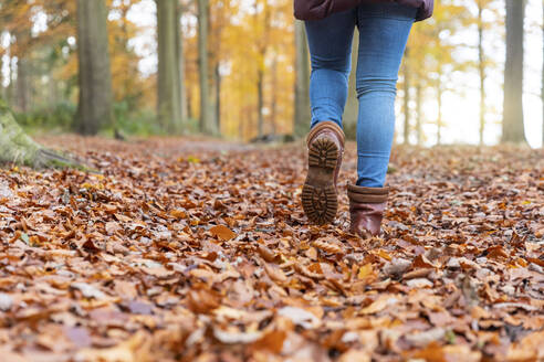 Frau mit Stiefeln läuft auf Herbstblättern im Wald - WPEF04193