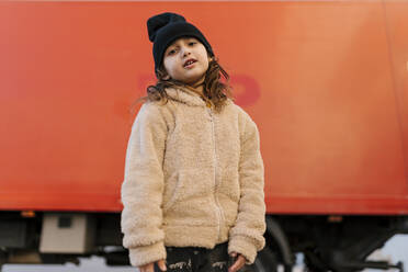 Nettes Mädchen mit Strickmütze und Pullover, das vor einem roten Lastwagen steht - EGAF01929
