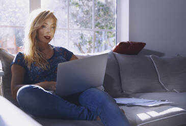 Frau benutzt Laptop, während sie zu Hause auf dem Sofa sitzt - AZF00194