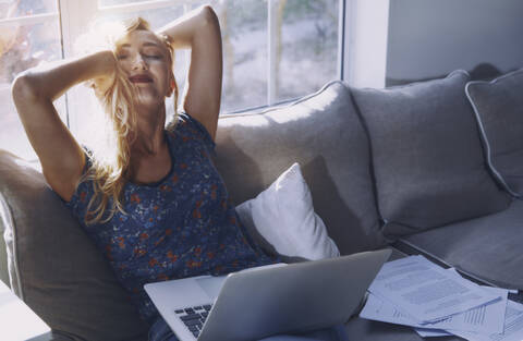 Frau ruht sich aus, während sie mit ihrem Laptop auf dem Sofa zu Hause sitzt, lizenzfreies Stockfoto