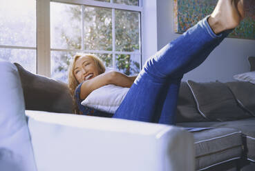 Happy woman embracing pillow while resting on sofa at home - AZF00198