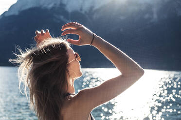 Woman with arms raised looking at view at Eibsee lake during sunny day - WFF00455