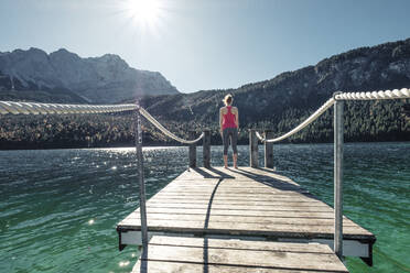 Young woman looking away while standing on pier at Eibsee lake - WFF00467