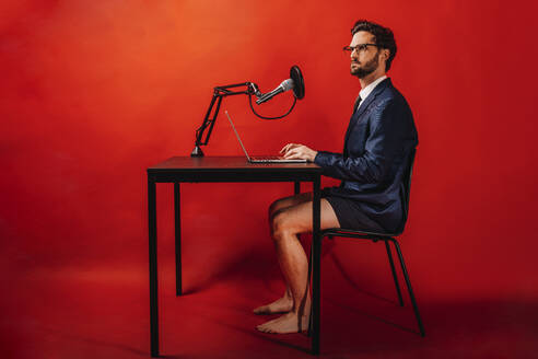 Businessman using laptop at desk by red background - DAWF01872