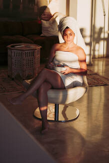 Entspannte Frau im Handtuch mit Obstschale, die wegschaut, während sie auf einem Stuhl zu Hause sitzt - LJF02061