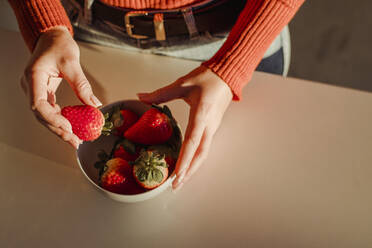 Frau hält frische Erdbeeren am Esstisch zu Hause - LJF02072