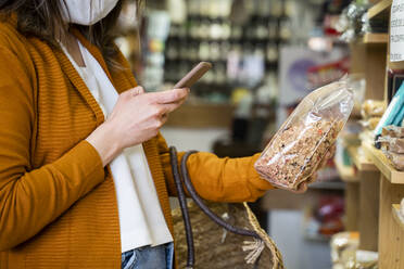 Junge Frau fotografiert Bio-Lebensmittel-Paket in einem Lebensmittelladen - AFVF08306