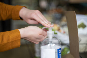 Woman disinfecting hands using sanitizer at store - AFVF08309