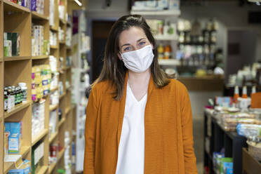 Young woman wearing protective face mask standing in grocery store - AFVF08310