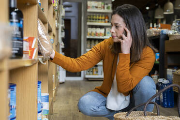 Junge Frau telefoniert beim Lebensmitteleinkauf im Laden - AFVF08312