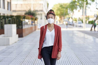 Junge Frau mit Kopftuch und Gesichtsschutzmaske auf dem Gehweg - KIJF03619