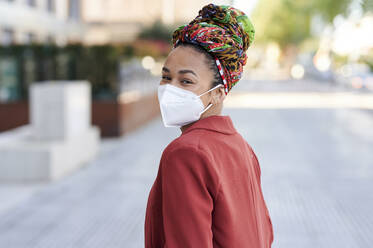 Woman wearing protective face mask staring while standing outdoors - KIJF03620