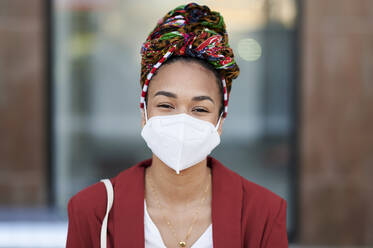 Woman wearing protective face mask and headscarf staring while standing outdoors - KIJF03622