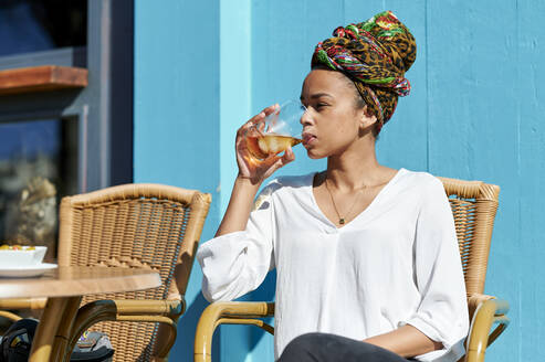 Frau mit Kopftuch trinkt Alkohol, während sie an einer Bar sitzt - KIJF03630
