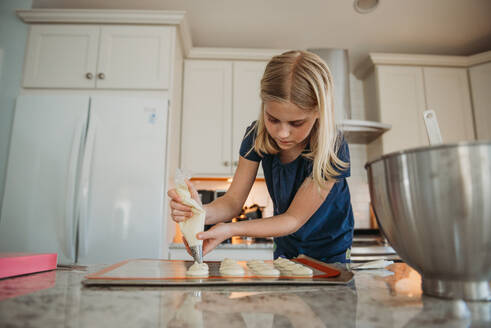 Young girl piping macarons in kitchen - CAVF93451