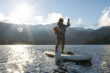 Paddle boarding with life jacket on lake against snowy mountain ridge - CAVF93466