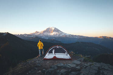 Ein Mann steht bei einem Zelt auf dem Gipfel eines Berges in der Nähe des Mount Rainier - CAVF93482