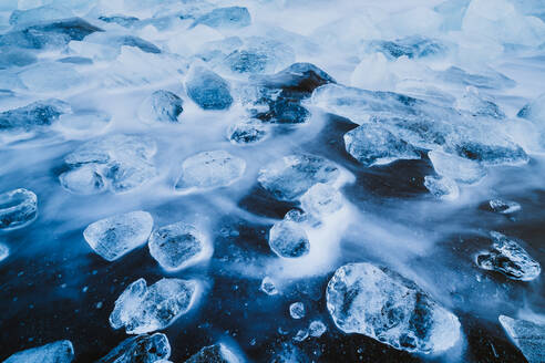 Langzeitbelichtung von Wasser, das durch Eisblöcke am schwarzen Sandstrand fließt - CAVF93485