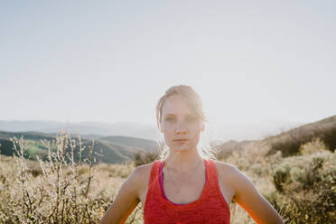 Athletic blonde woman stares back at you with sun and mountains behind - CAVF93524