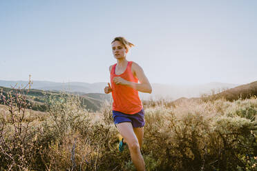 Athletic blonde woman trail runs in the mountains at golden hour - CAVF93526