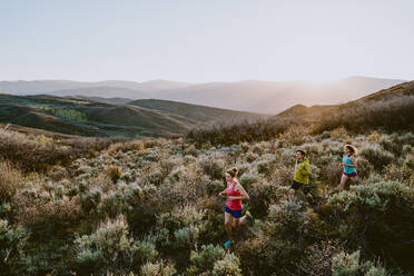 Three friends trail running in the mountains at golden hour - CAVF93527