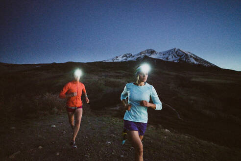 Two women run at night in the mountains wearing headlamps - CAVF93528