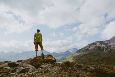 A man standing on rocky summit looks out at mountain view - CAVF93533