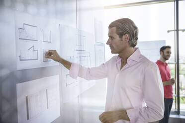 Selbstbewusster männlicher Architekt bei der Arbeit mit einem Diagramm am weißen Brett im Büro - BMOF00511