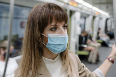 Woman with protective face mask looking away while traveling by subway train during pandemic - AMPF00045