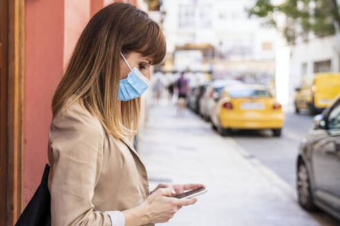 Brown hair woman using mobile phone while waiting for taxi during COVID-19 - AMPF00049