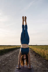 Woman doing handstand against sky on road - AMPF00071