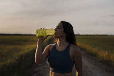 Woman drinking water through bottle against sky - AMPF00077