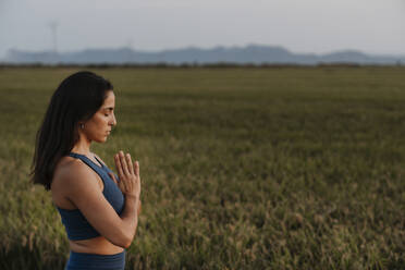 Woman with hands clasped standing at meadow - AMPF00081